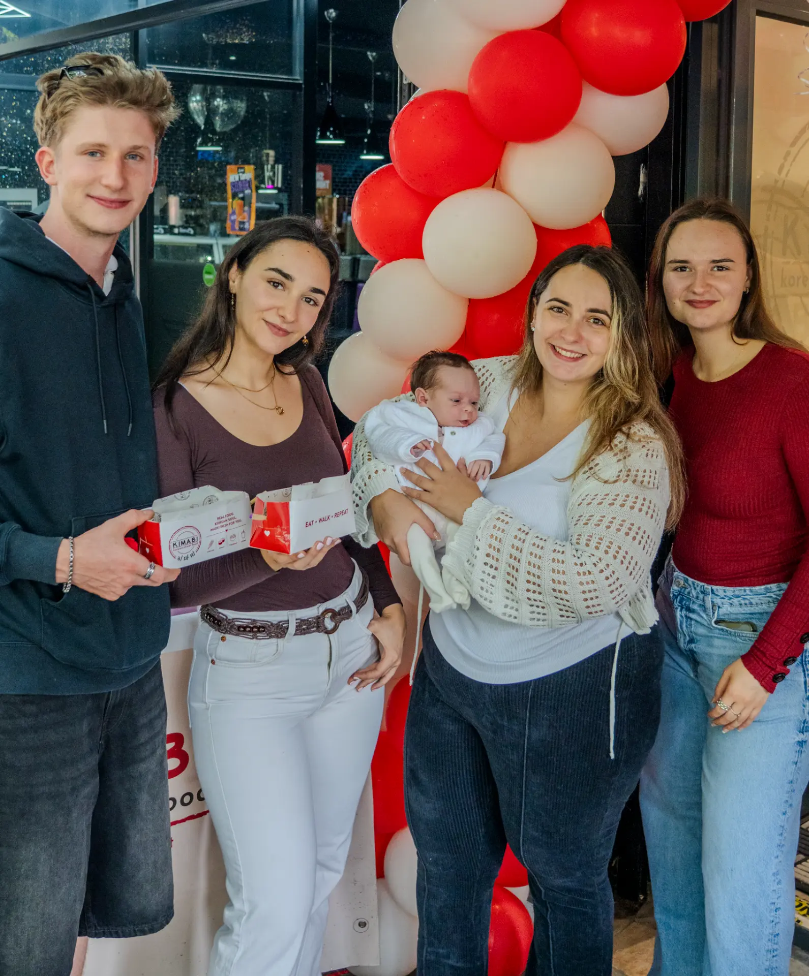 Group of friends with Kimabi boxes in front of red and white balloons