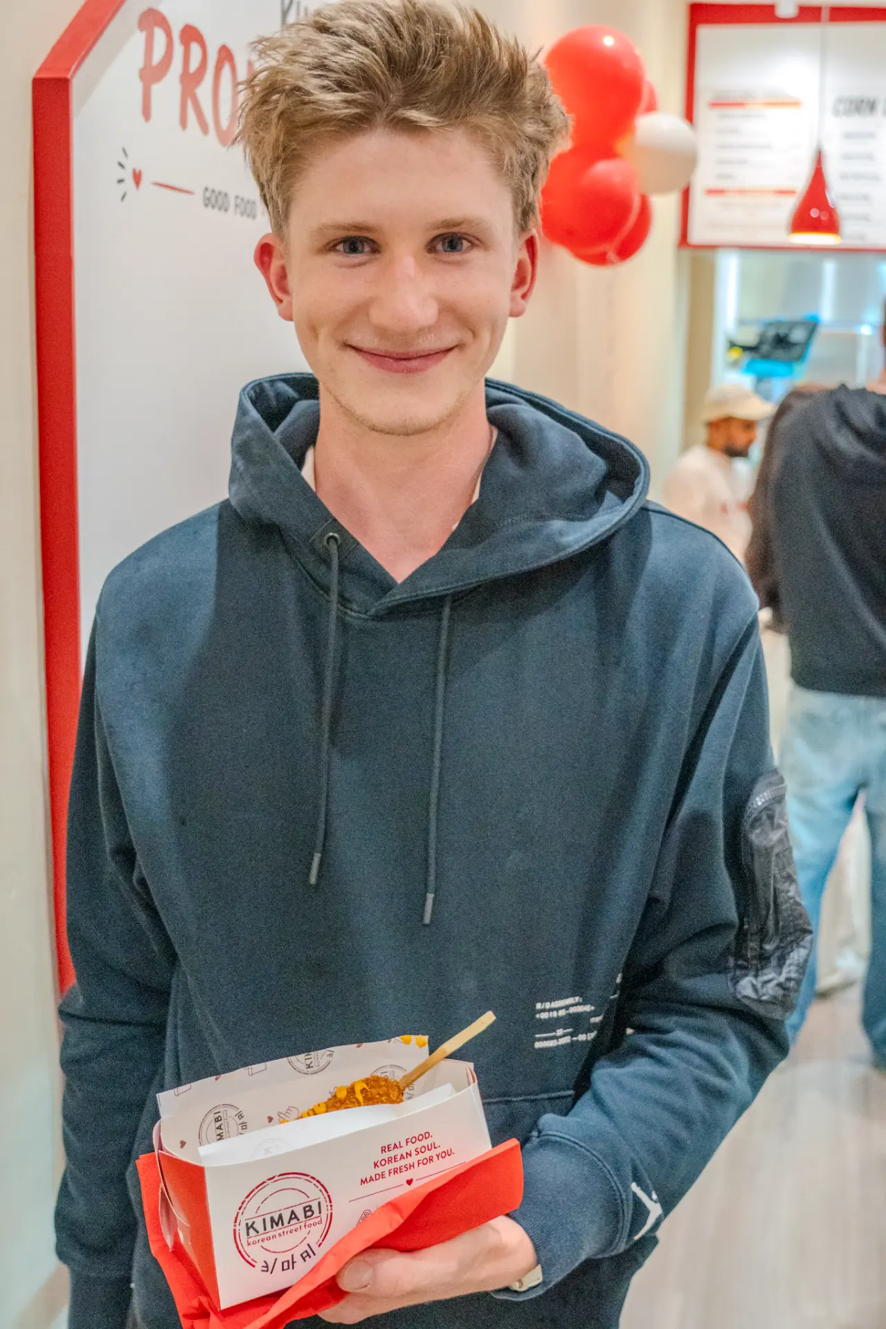 Guest smiling with a Kimabi cupbap box by the promise wall